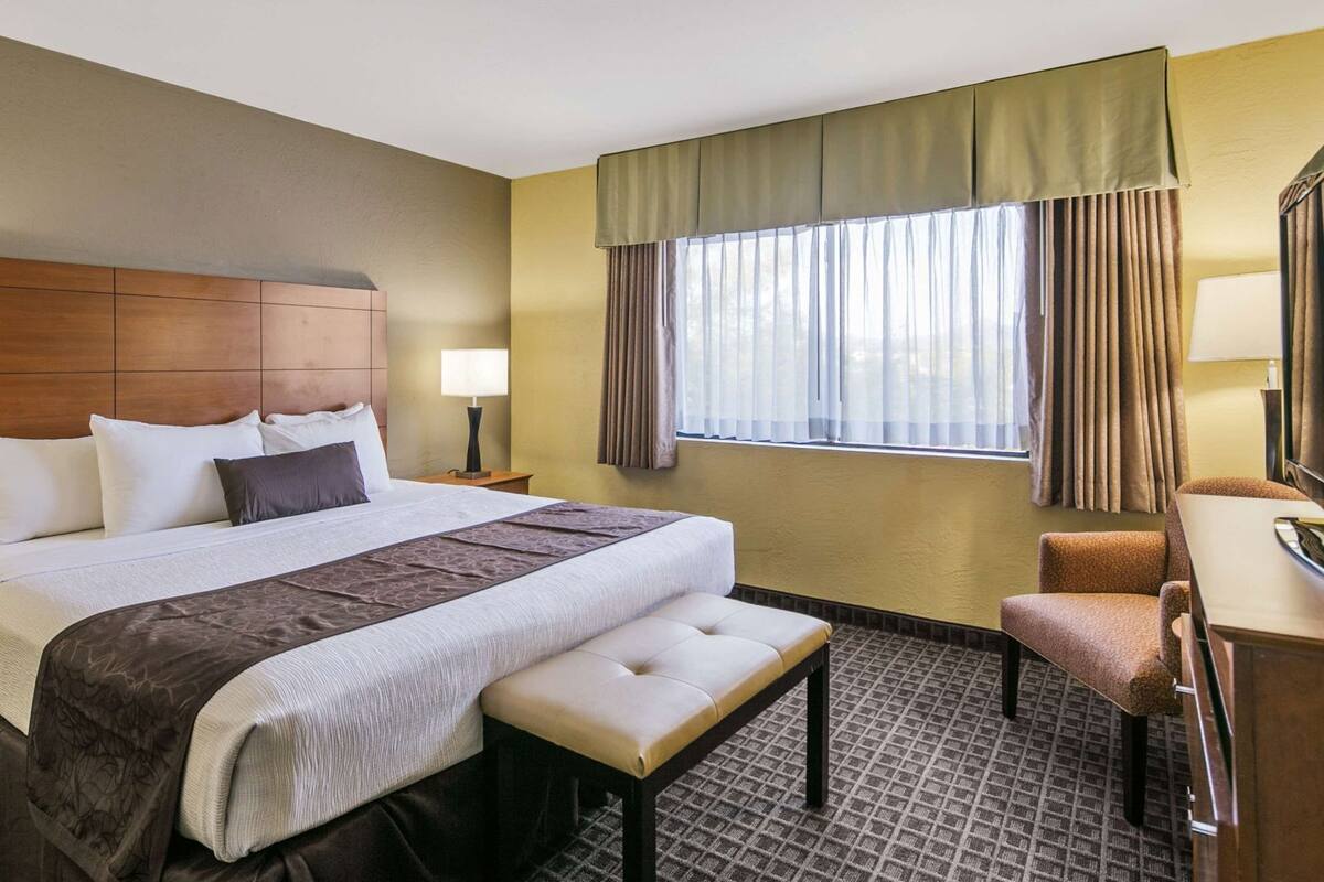 A hotel room with a large bed, a desk, a chair, a window with curtains, and a headboard.