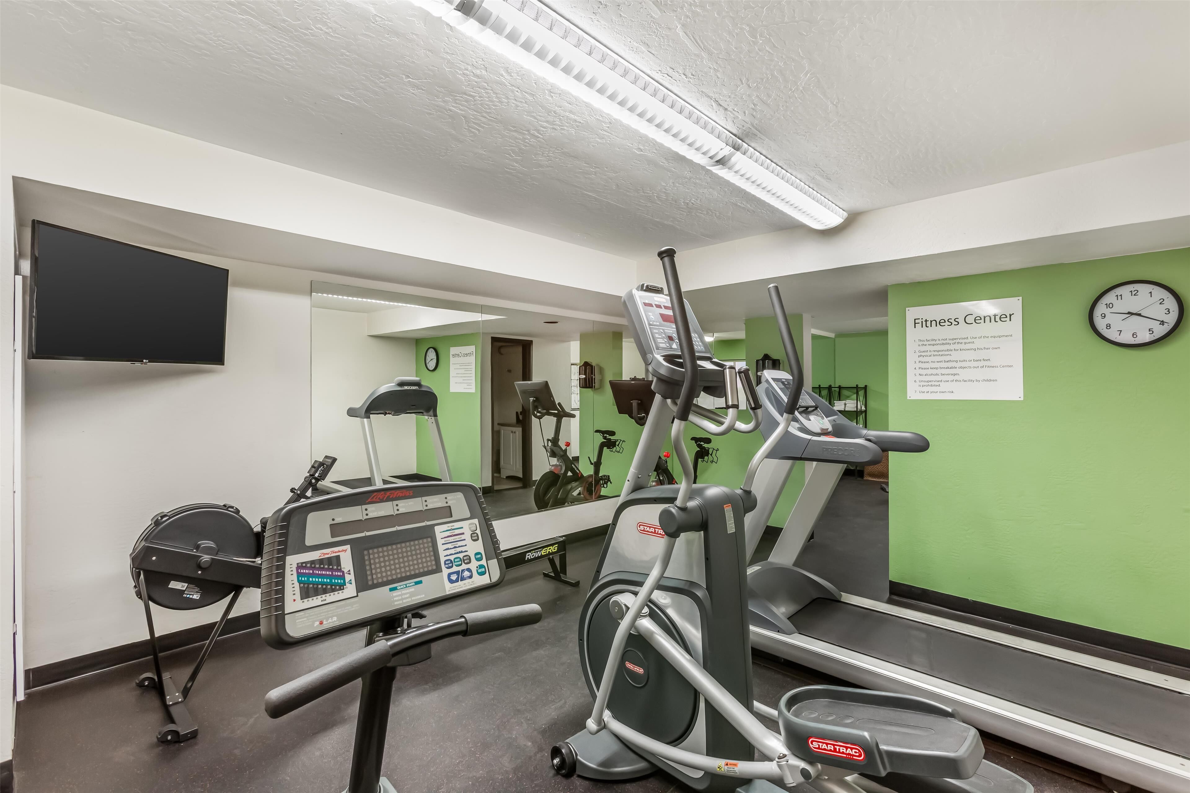 A fitness center with exercise equipment, a mirror, a clock, and a sign.