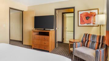 A hotel room with a bed, a wooden dresser with a television, a striped armchair, a small table, and a framed picture on the wall.