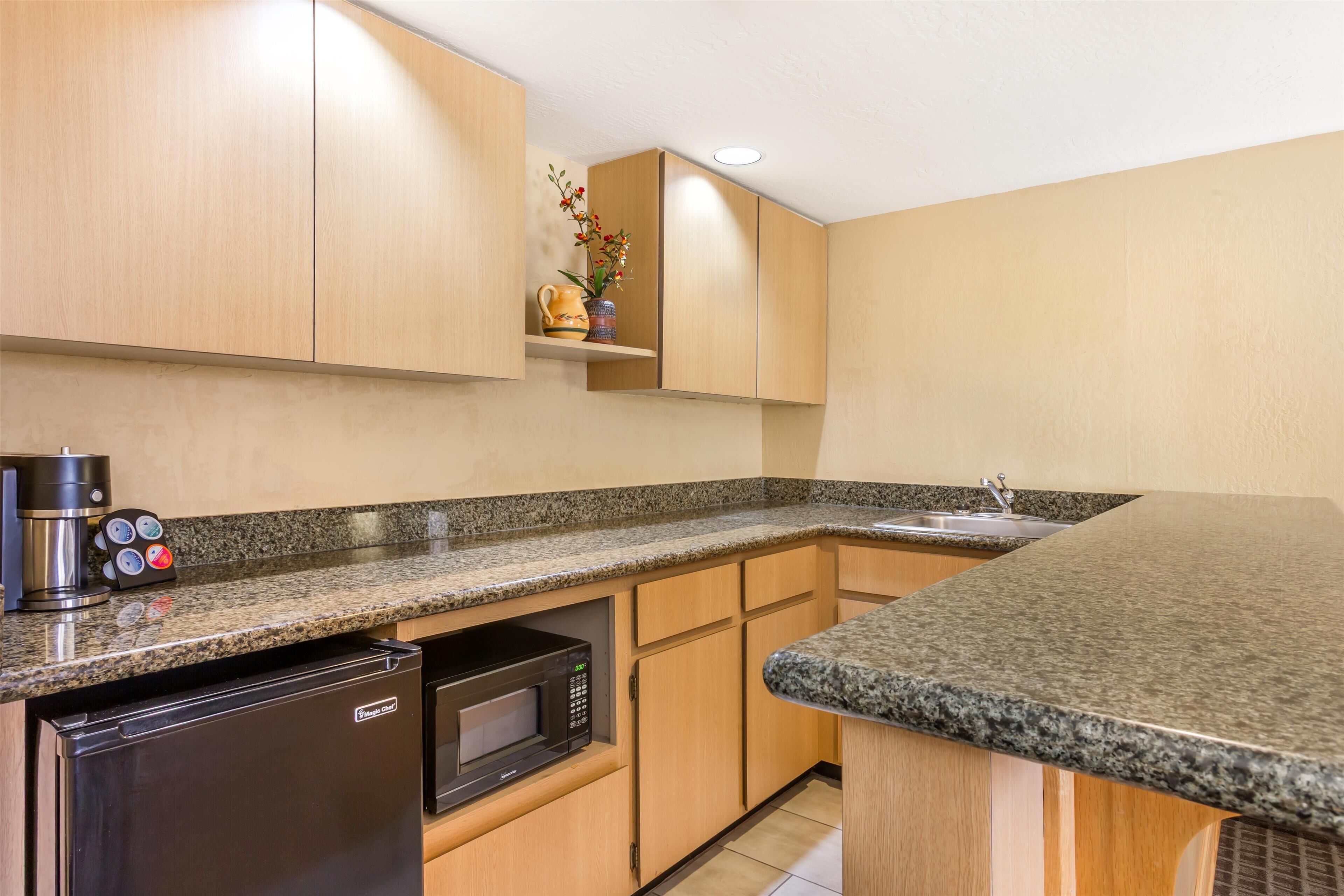 A kitchen with granite countertops, wooden cabinets, a built-in microwave, a coffee maker, and a sink.