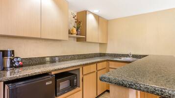 A kitchen with granite countertops, wooden cabinets, a built-in microwave, a coffee maker, and a sink.
