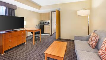 A hotel room with a TV, wooden desk, sofa, and a lamp.