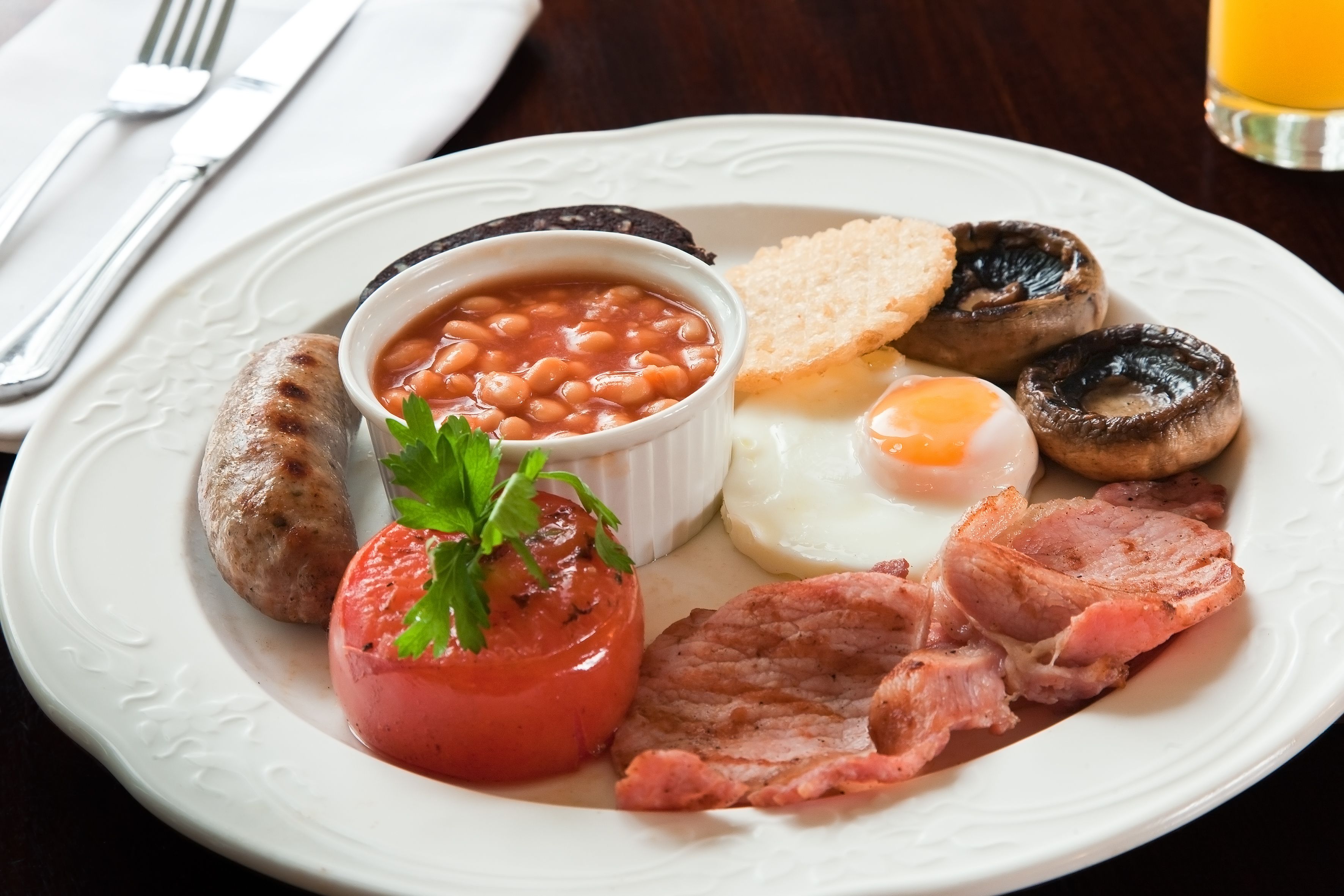 A plate of breakfast food including sausages, eggs, beans, mushrooms, bacon, and toast.