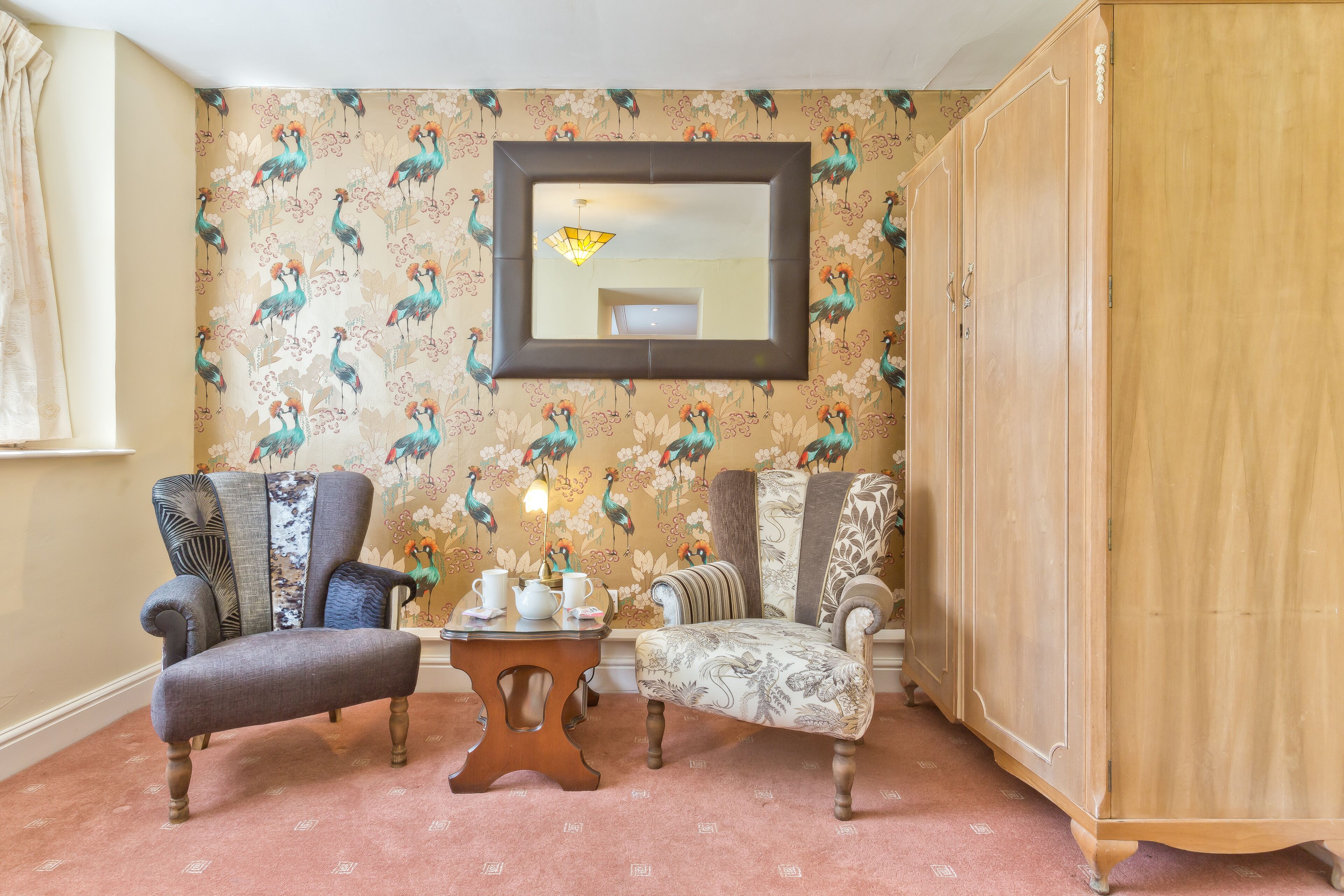 Een kamer met twee fauteuils, een tafeltje en een spiegel aan de wand.