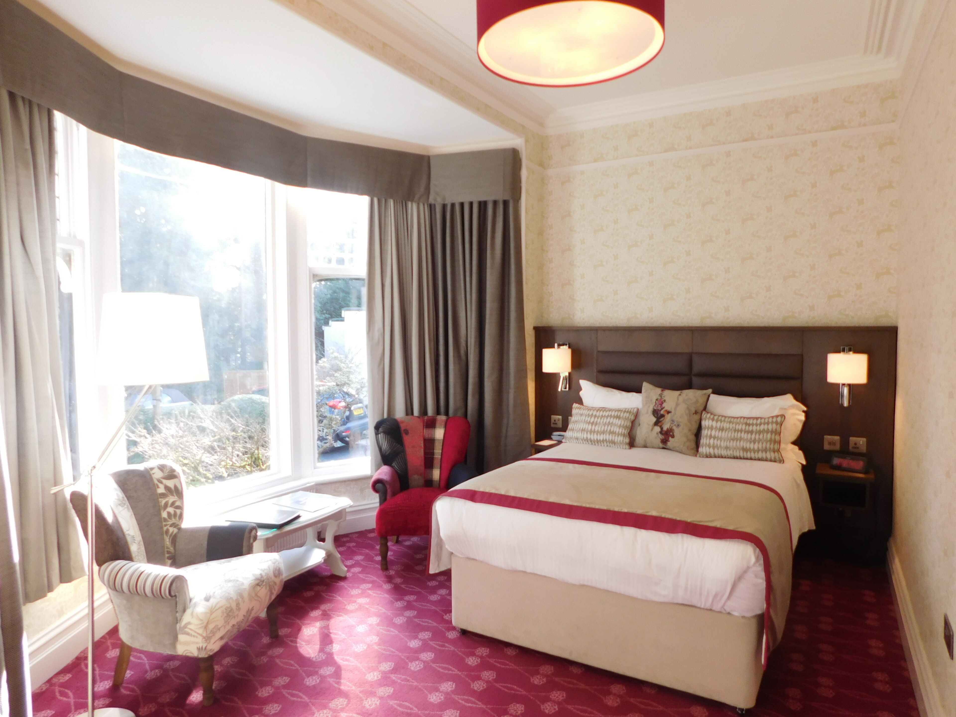 A hotel room with a large bed, a chair, a small table, and a window with curtains.