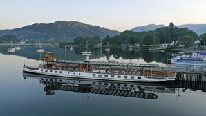 A riverboat docked at a pier with a view of a forested hillside in the background. - The Burn How Garden House Hotel (Windermere)