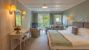 A hotel room with a bed, desk, chair, TV, and a view of the outdoors. - The Burn How Garden House Hotel (Windermere)