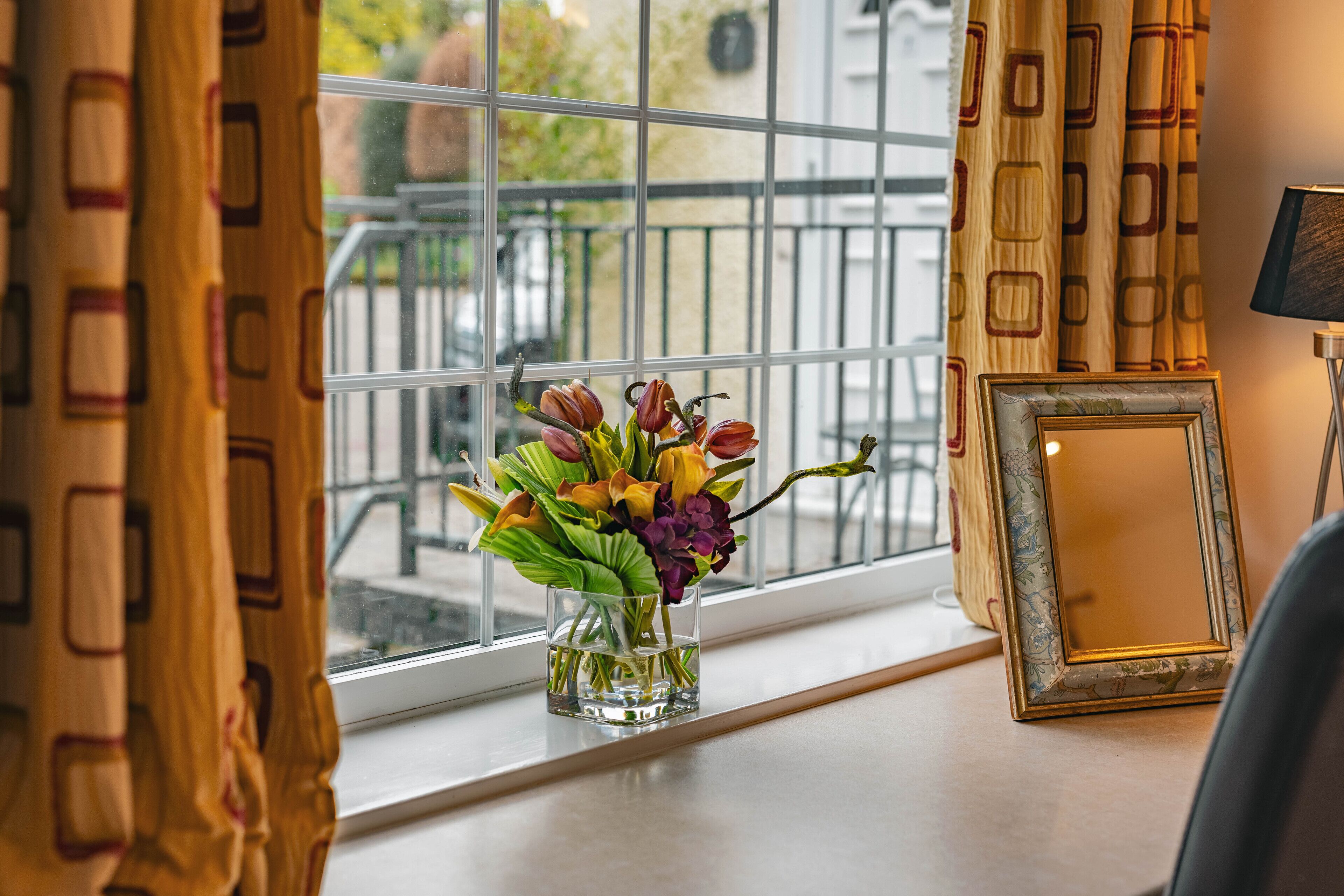 A window with a vase of flowers, a framed picture, and curtains.
