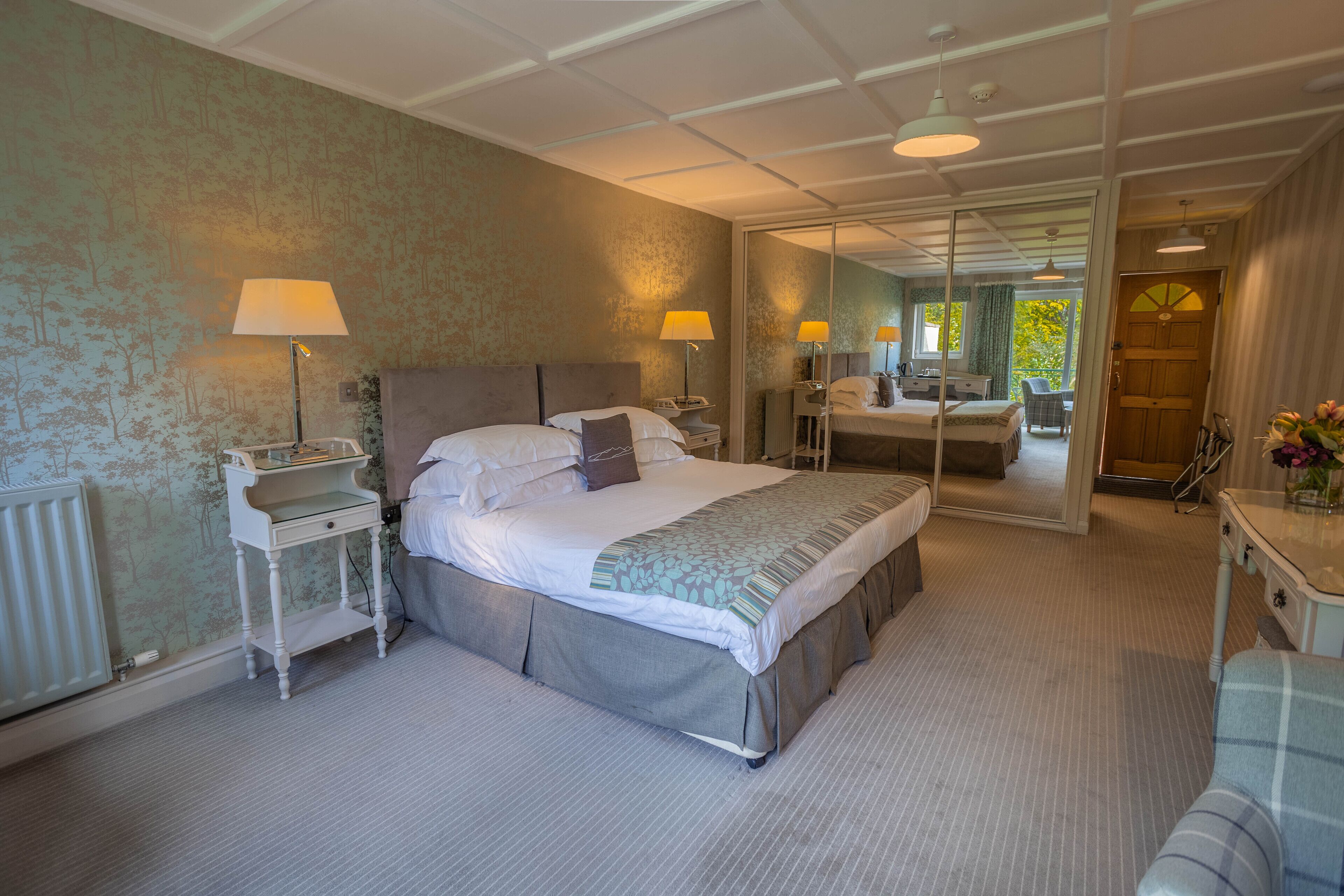 Une chambre d’hôtel avec un grand lit, des tables de chevet, un miroir et une vue sur l’extérieur.