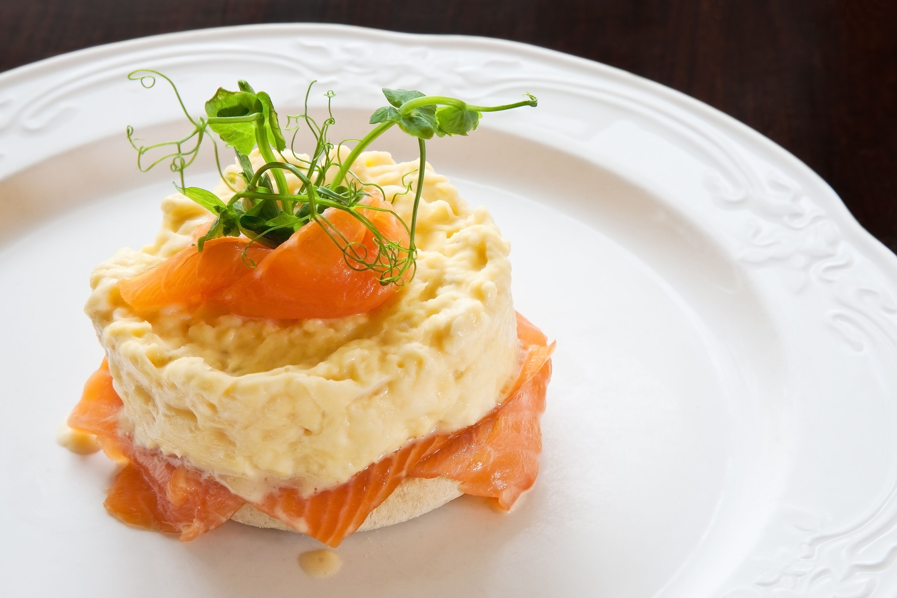 A dish with a creamy base, topped with smoked salmon and garnished with greens.