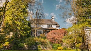 A large house with a stone wall and a well-maintained garden. - The Burn How Garden House Hotel (Windermere)