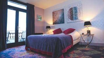 A hotel room with a bed, two side tables with lamps, a balcony view, and artwork on the wall.
