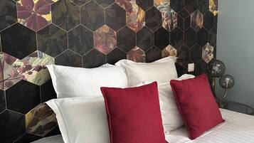 A bed with white and red pillows, a dark hexagonal patterned headboard, and a bedside table with a lamp.