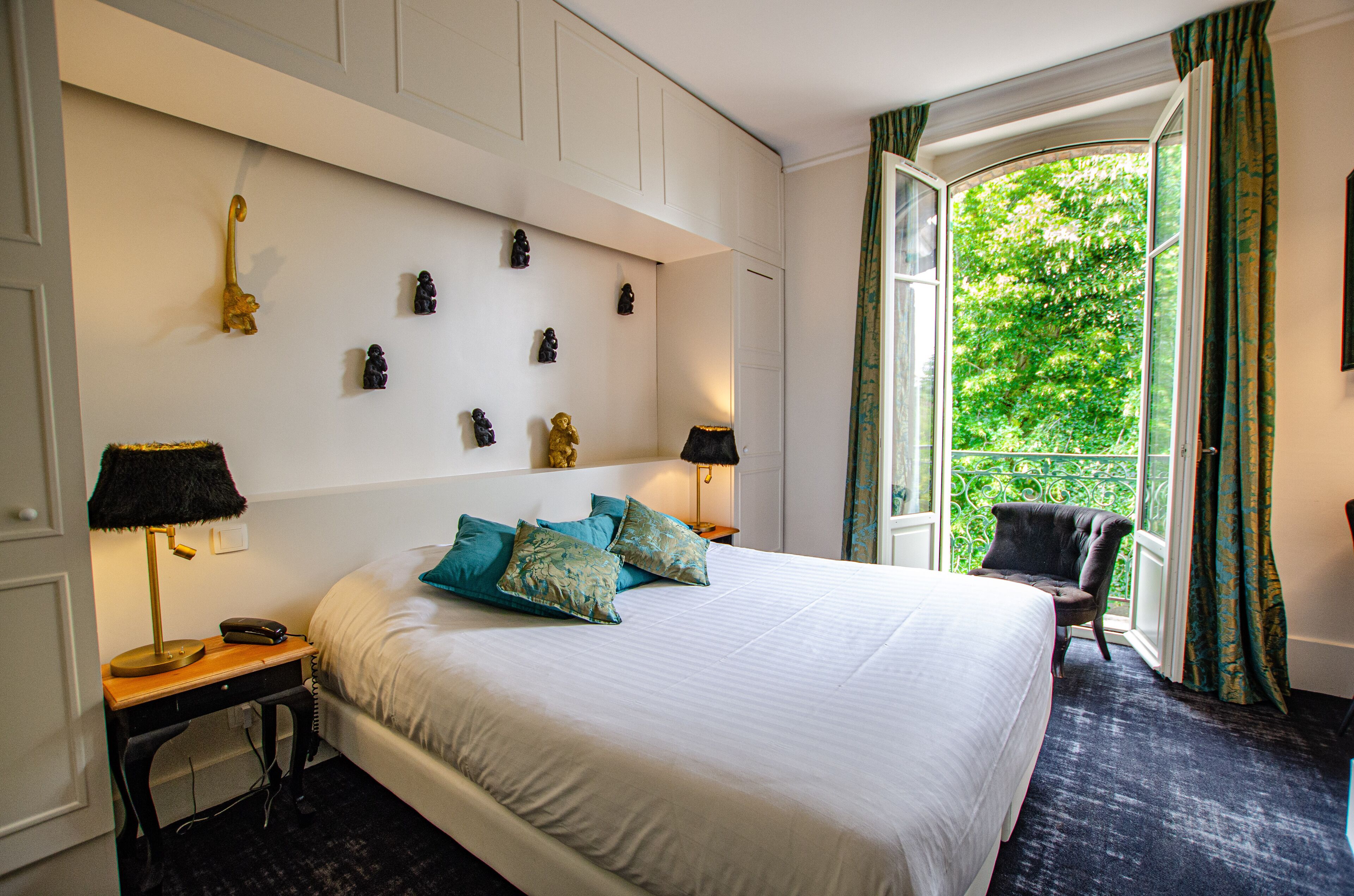 Habitación de hotel con una cama grande, una mesita de noche con lámpara, una silla y una ventana con cortinas.