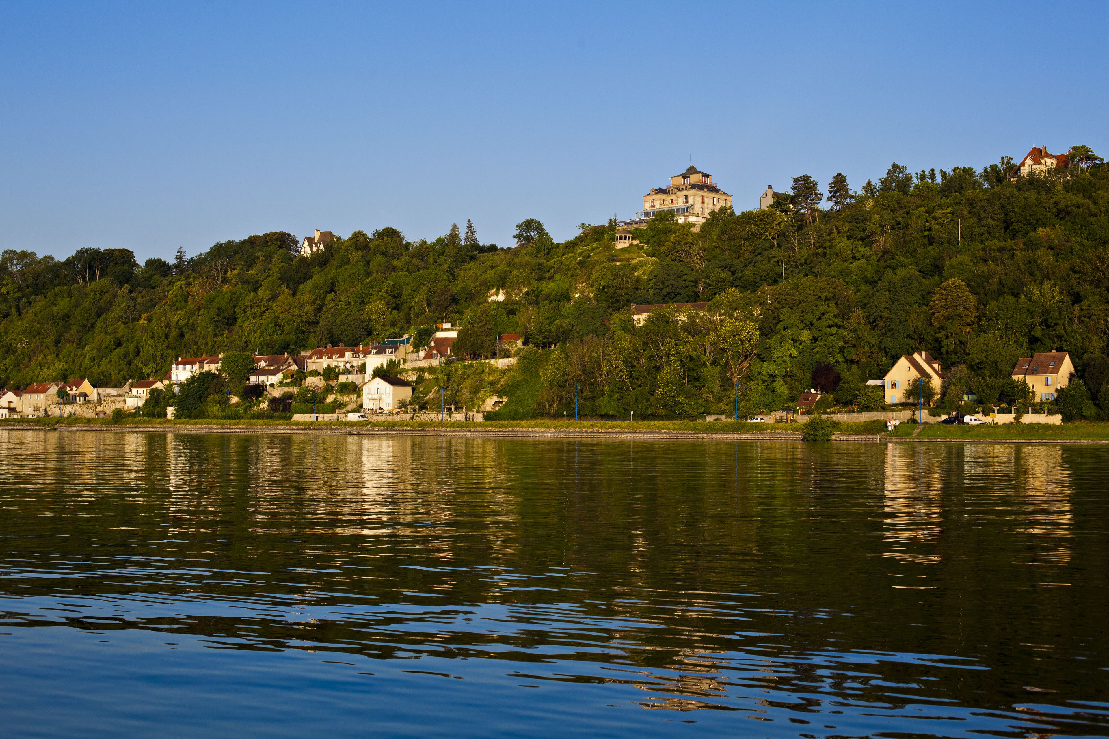 A lakeside view with a hilltop building and surrounding houses.