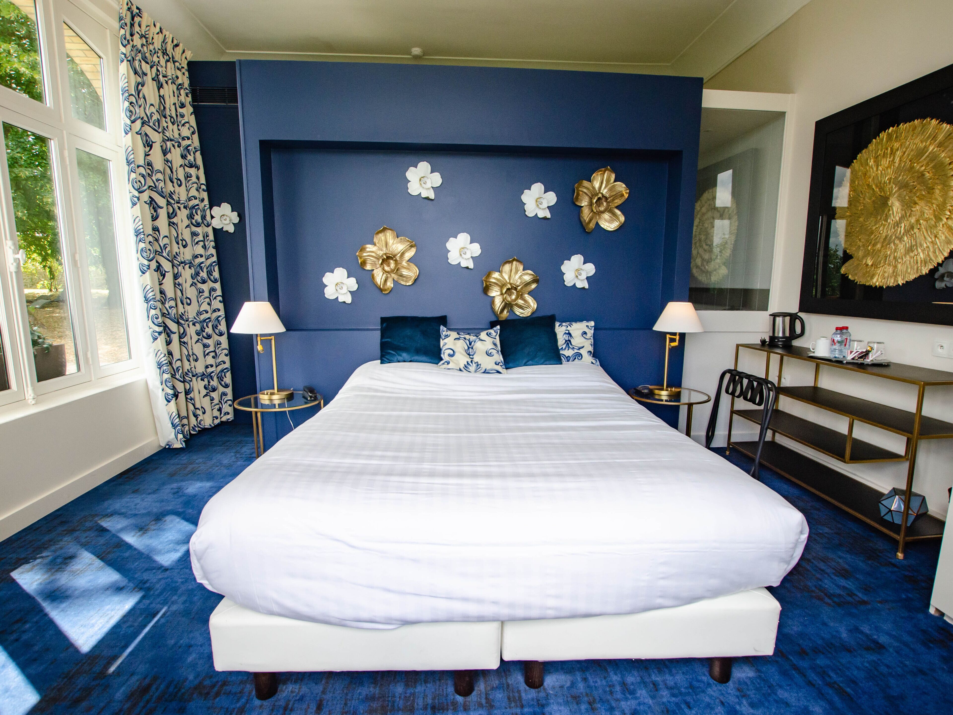 A large bed with white linens, a blue accent wall, and decorative gold and white flowers.