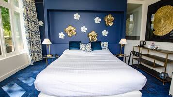 A large bed with white linens, a blue accent wall, and decorative gold and white flowers.