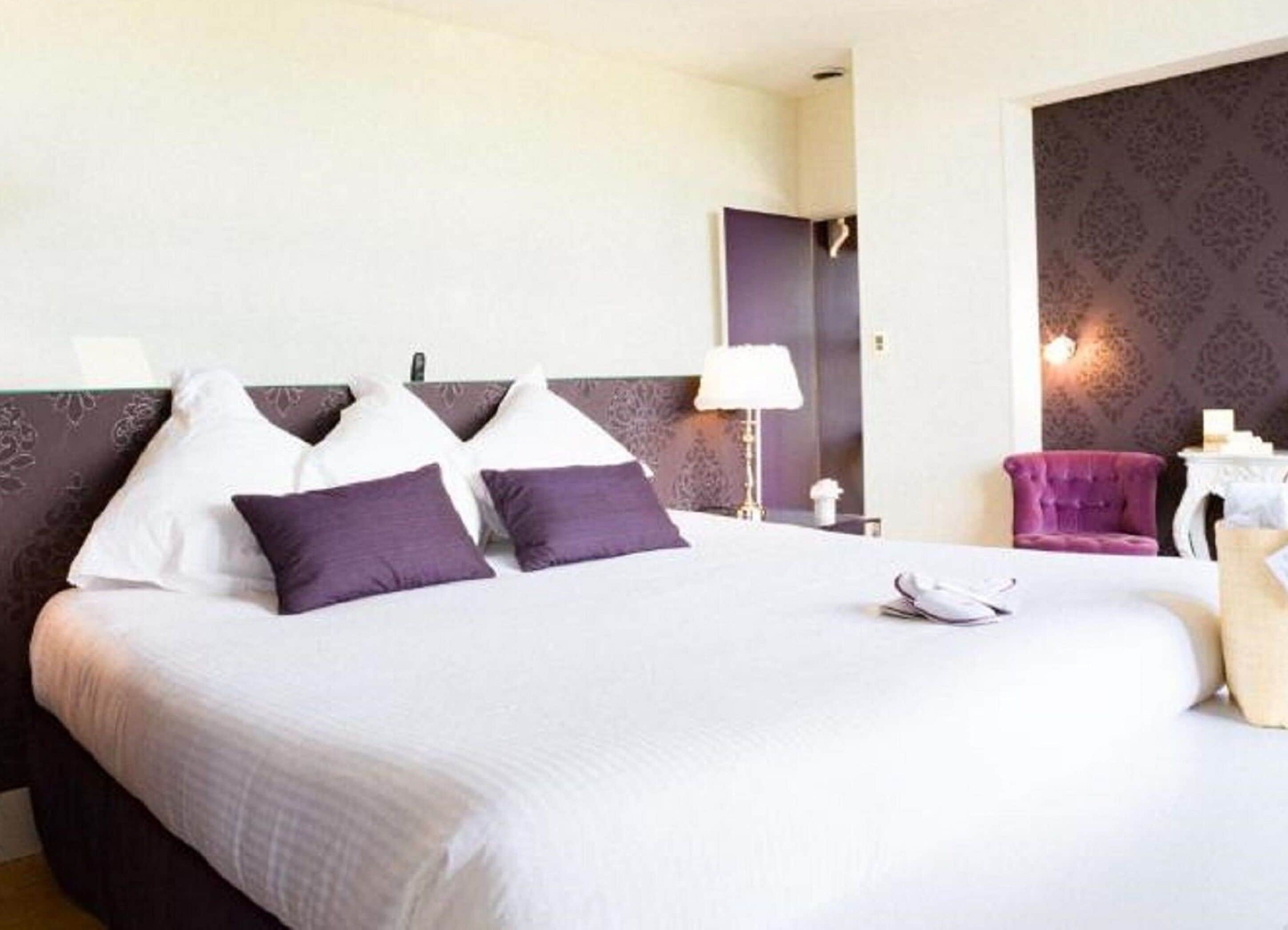Una habitación de hotel con una cama, lámpara de noche, una silla y un espejo.