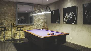 A pool table with balls, a mirror, and pool cues in a room with stone walls and artwork.