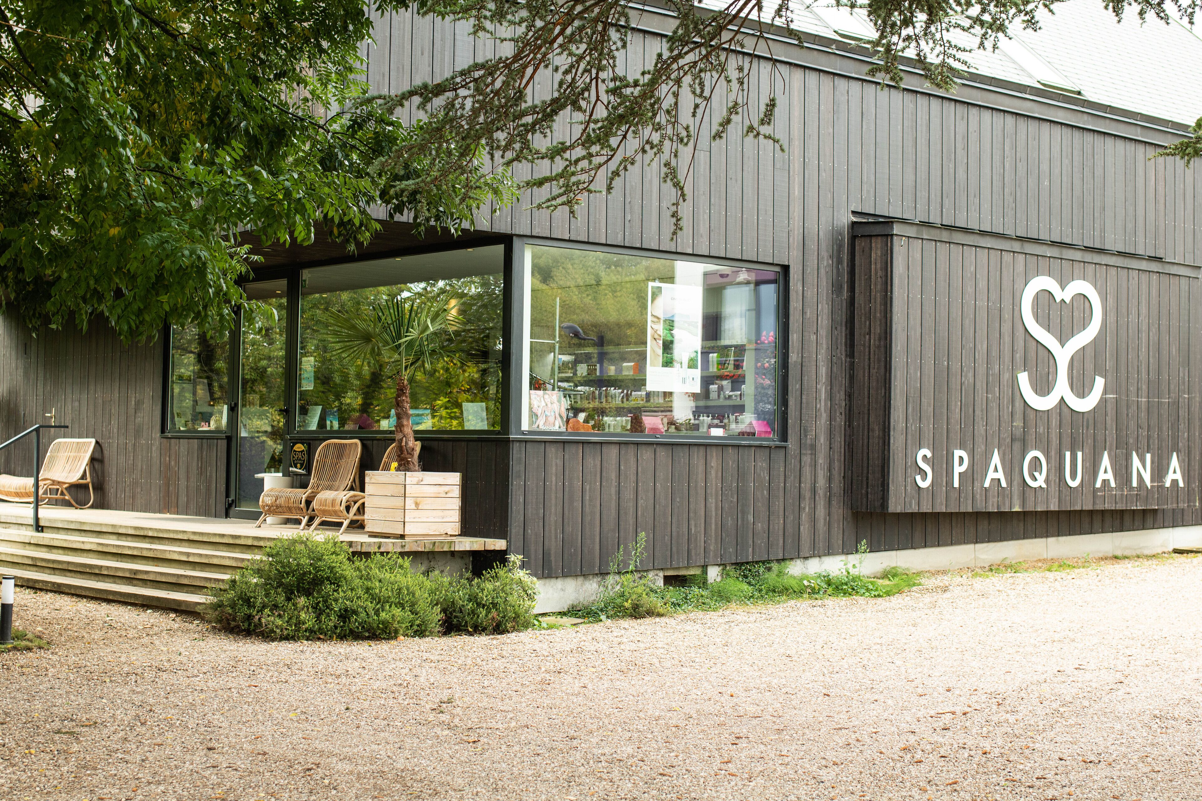 Un bâtiment abritant un spa, doté d’une grande baie vitrée, d’un escalier en bois et de fauteuils en osier à l’extérieur.