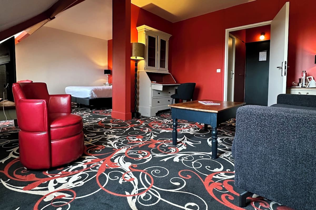 Ein Hotelzimmer mit einem Bett, einem roten Sessel, einem Schreibtisch mit einem Computer und einem grauen Sofa.