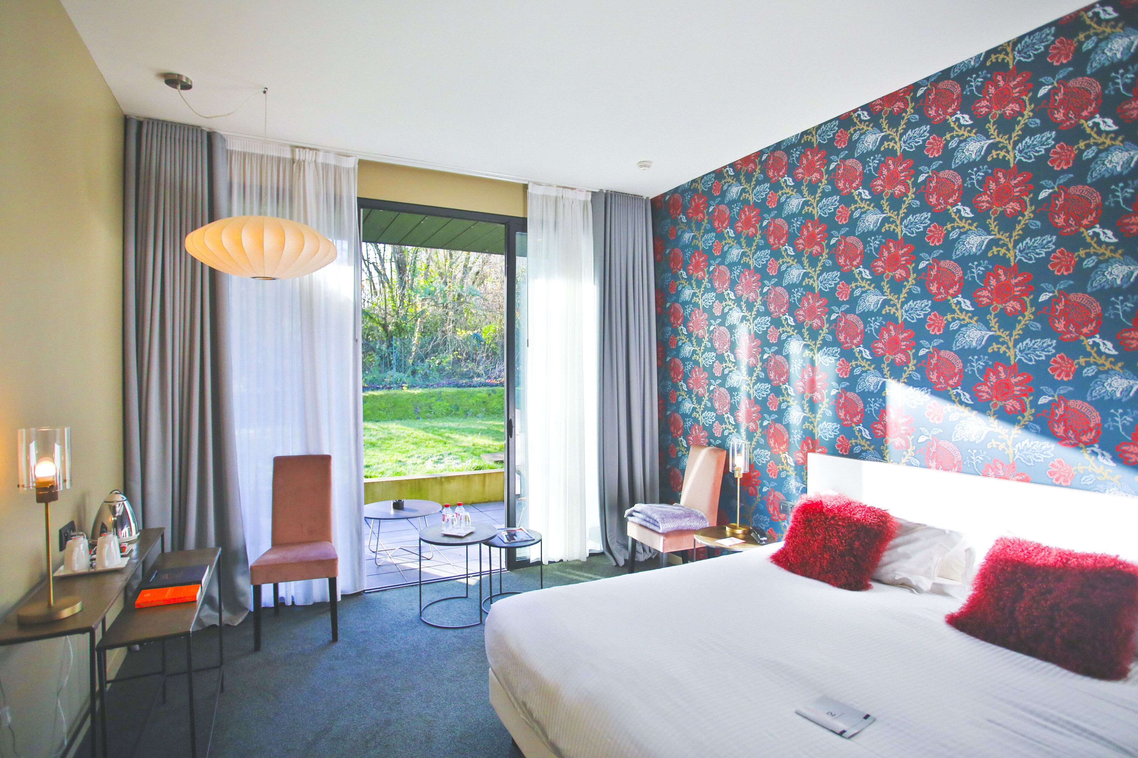 A hotel room with a large bed, a desk with a chair, a small table, and a view of the outdoors.
