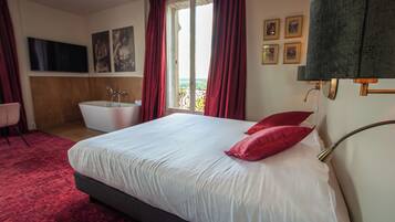 Habitación de hotel con una cama grande, una bañera y vistas al exterior.