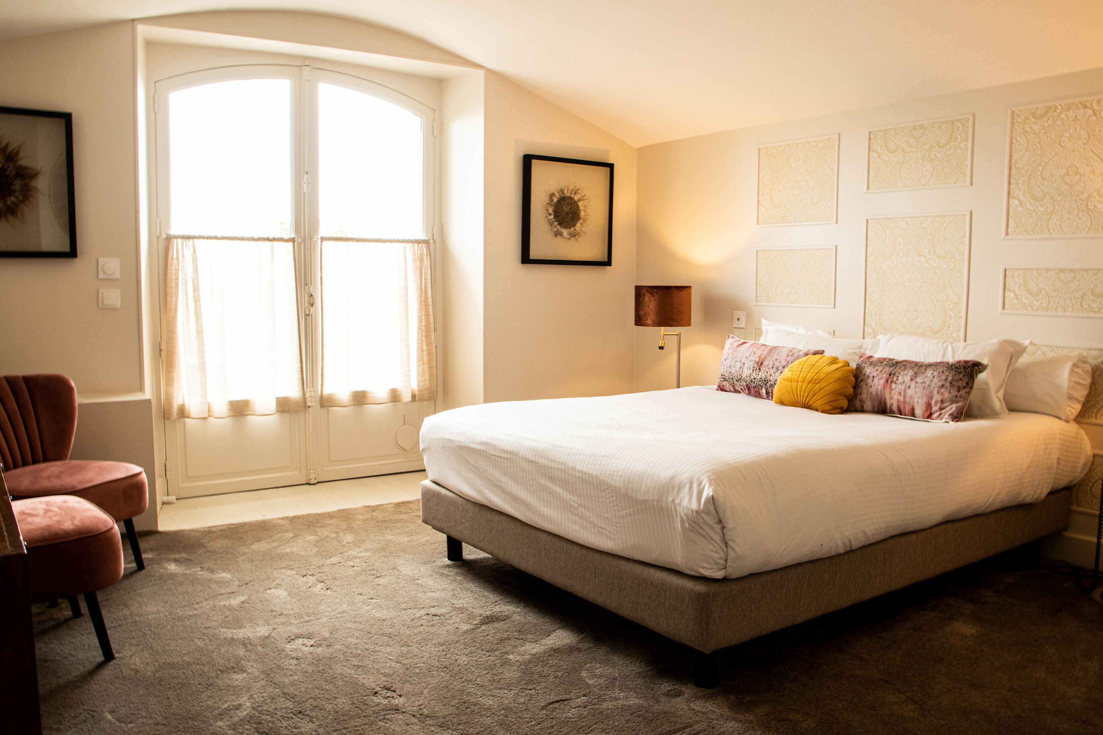 Una camera da letto con un letto grande, una sedia, una finestra con tende e un muro decorato con quadri.