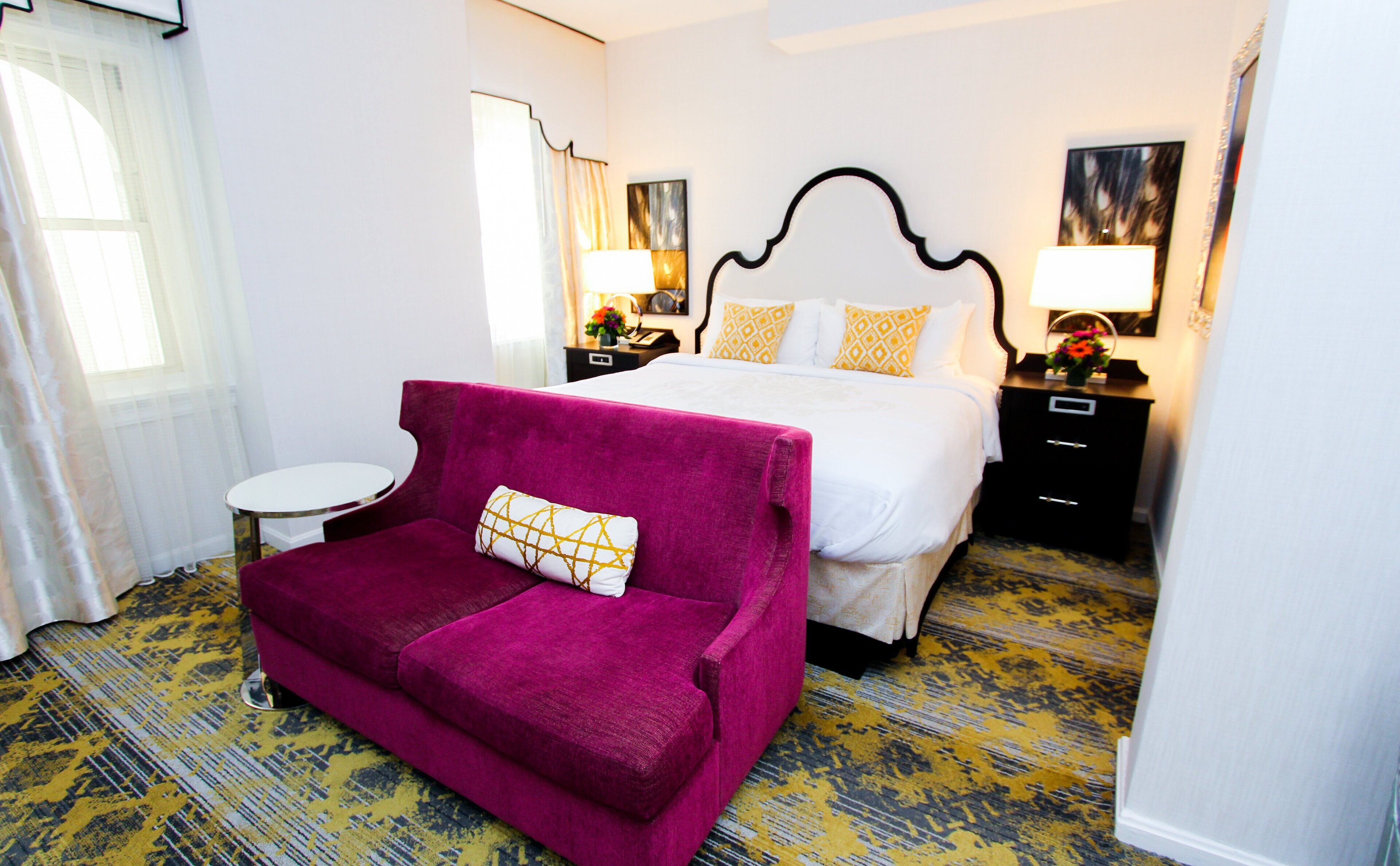 A hotel room with a large bed, a red sofa, a small round table, and a patterned carpet.