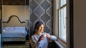 A room with a bed, a window with a curtain, and a wall with a geometric pattern.