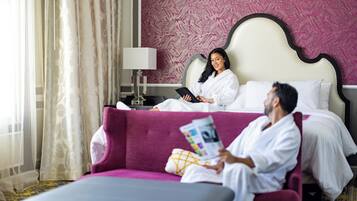 Une chambre d’hôtel avec un lit, une table de chevet avec une lampe, un canapé violet et une personne qui lit un magazine.