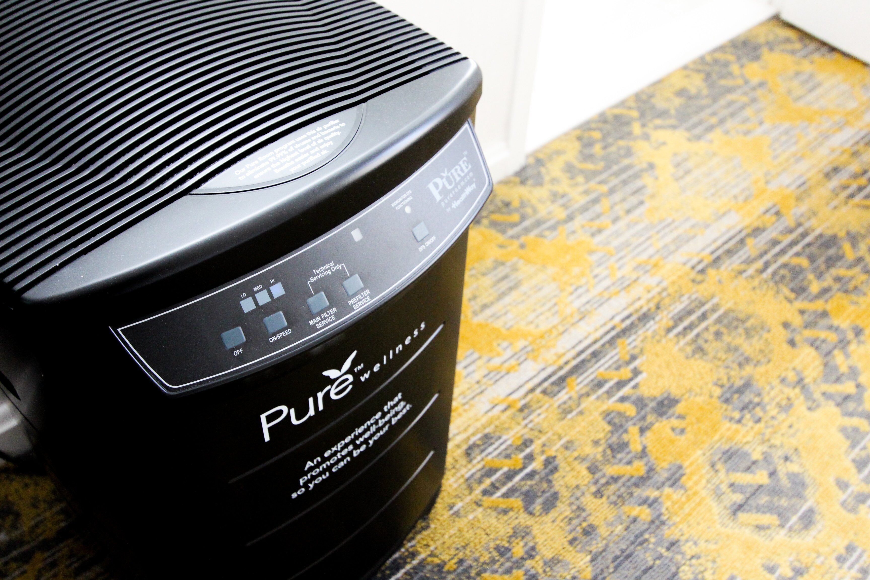 Um purificador de ar portátil preto, com painel de controle e a marca “Pure” visível na lateral.