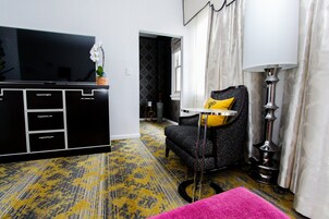 A modern living room with a black entertainment unit, a black sofa with a yellow pillow, a pink ottoman, and a floor lamp.