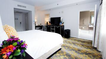 Une chambre d’hôtel avec un lit, un bureau, une télévision, une poubelle et une salle de bain visible à travers une porte ouverte.