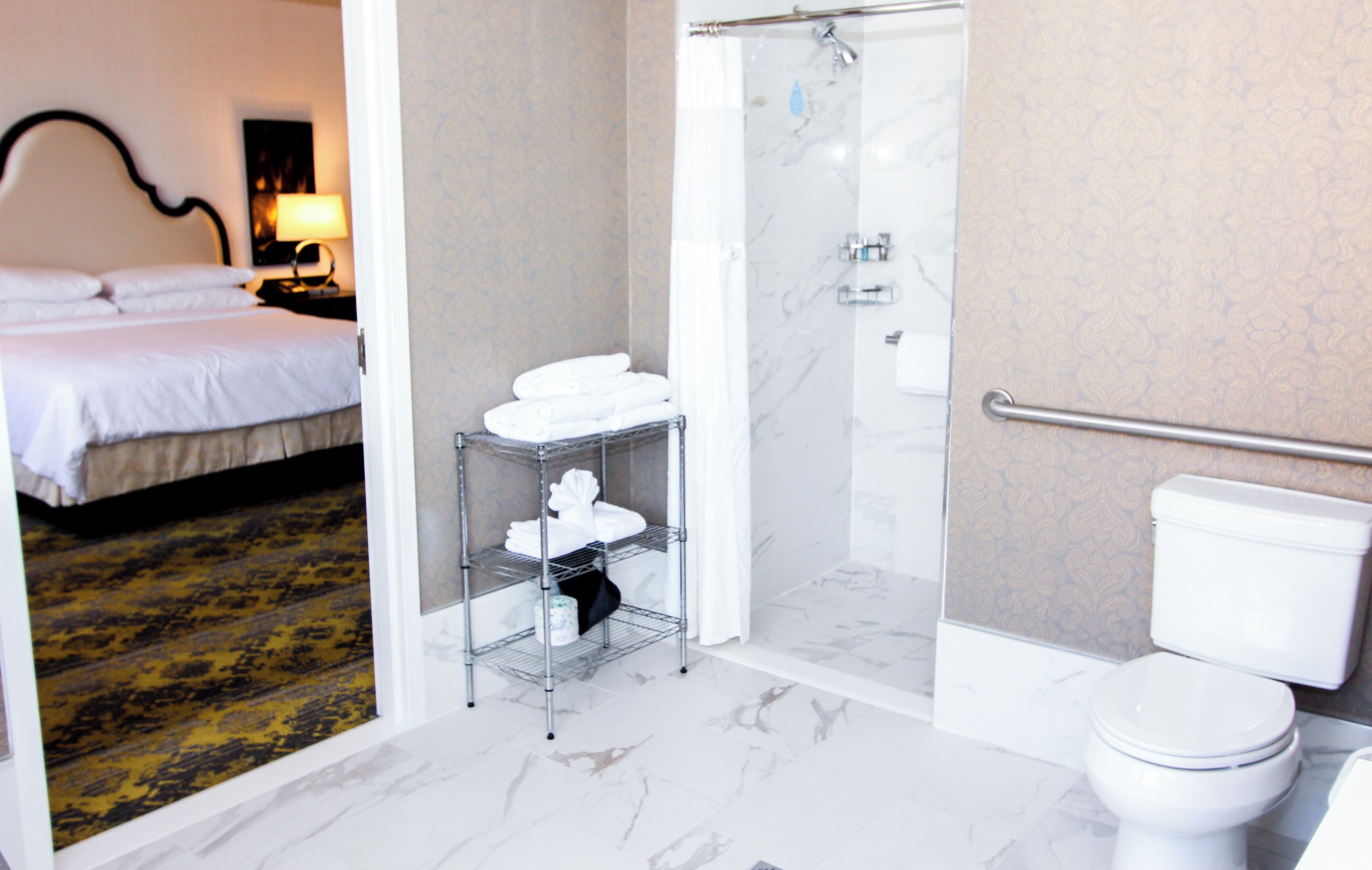 A hotel bathroom with a shower, toilet, and a shelf with towels.