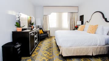 A hotel room with a bed, a desk, a chair, a dresser, and a window with curtains.