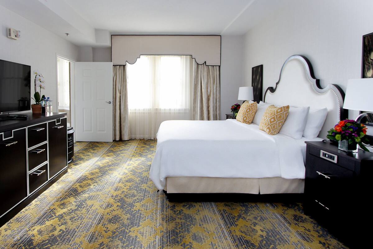 A hotel room with a bed, a TV, a dresser, and a window with curtains.