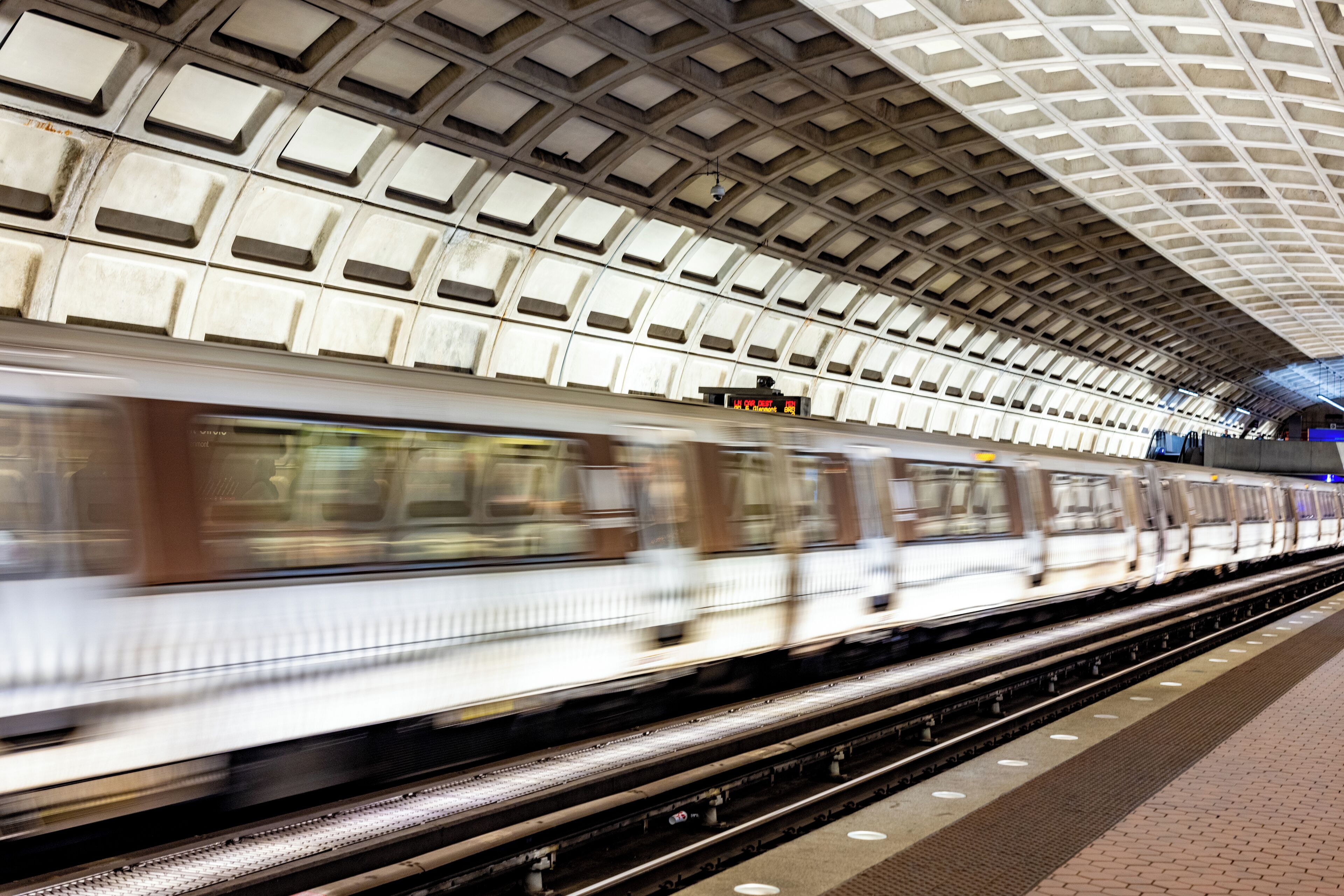 A subway station with a tiled ceiling and a moving train.