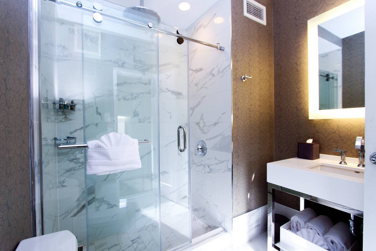 A modern bathroom with a glass-enclosed shower, a marble-tiled wall, a vanity with a mirror, and neatly folded towels.