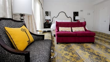 A hotel room with a bed, a red sofa, a yellow pillow, a black and white patterned chair, and a lamp.