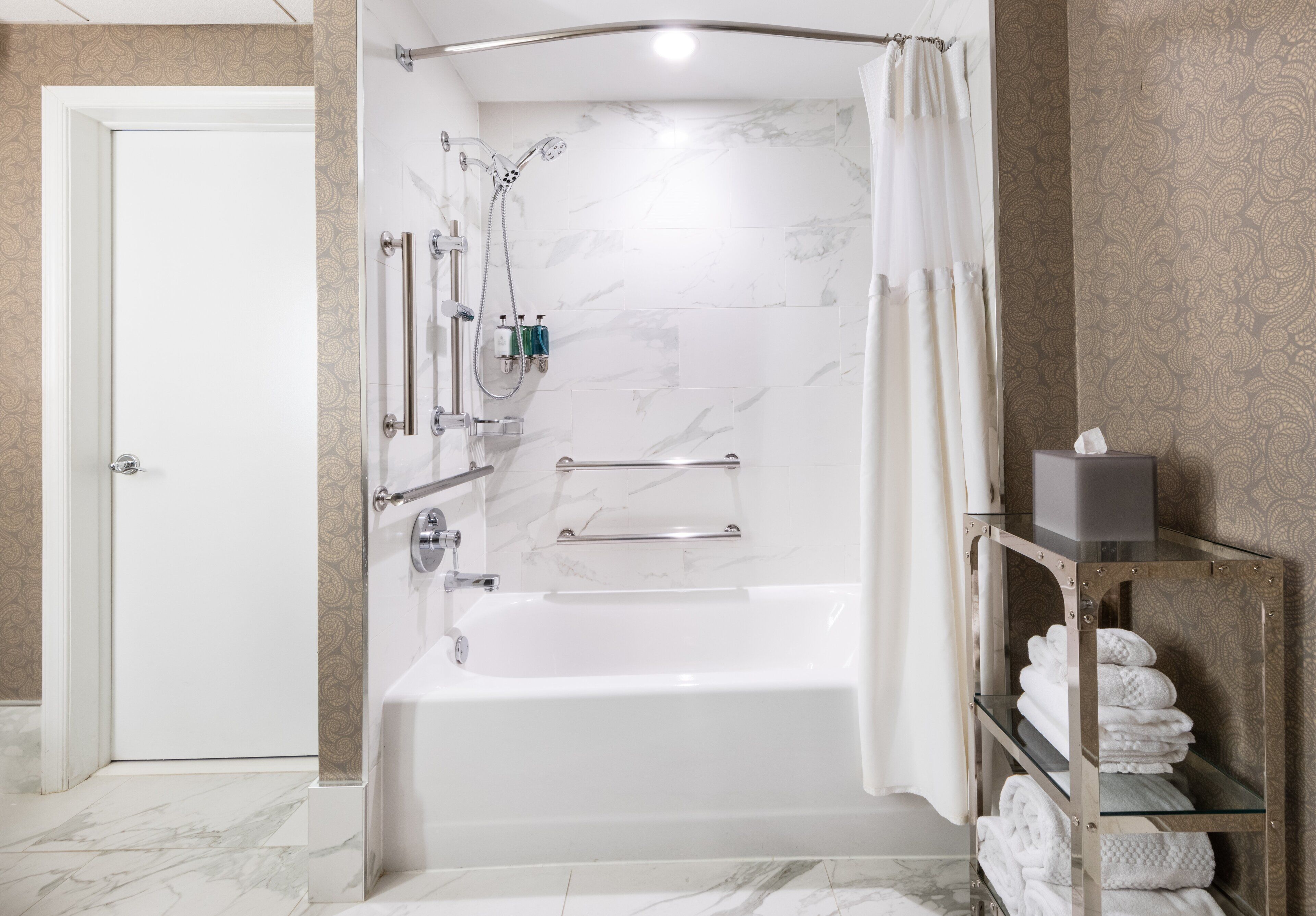 Une salle de bain moderne avec une baignoire, une douche et des étagères en verre où sont rangées les serviettes.