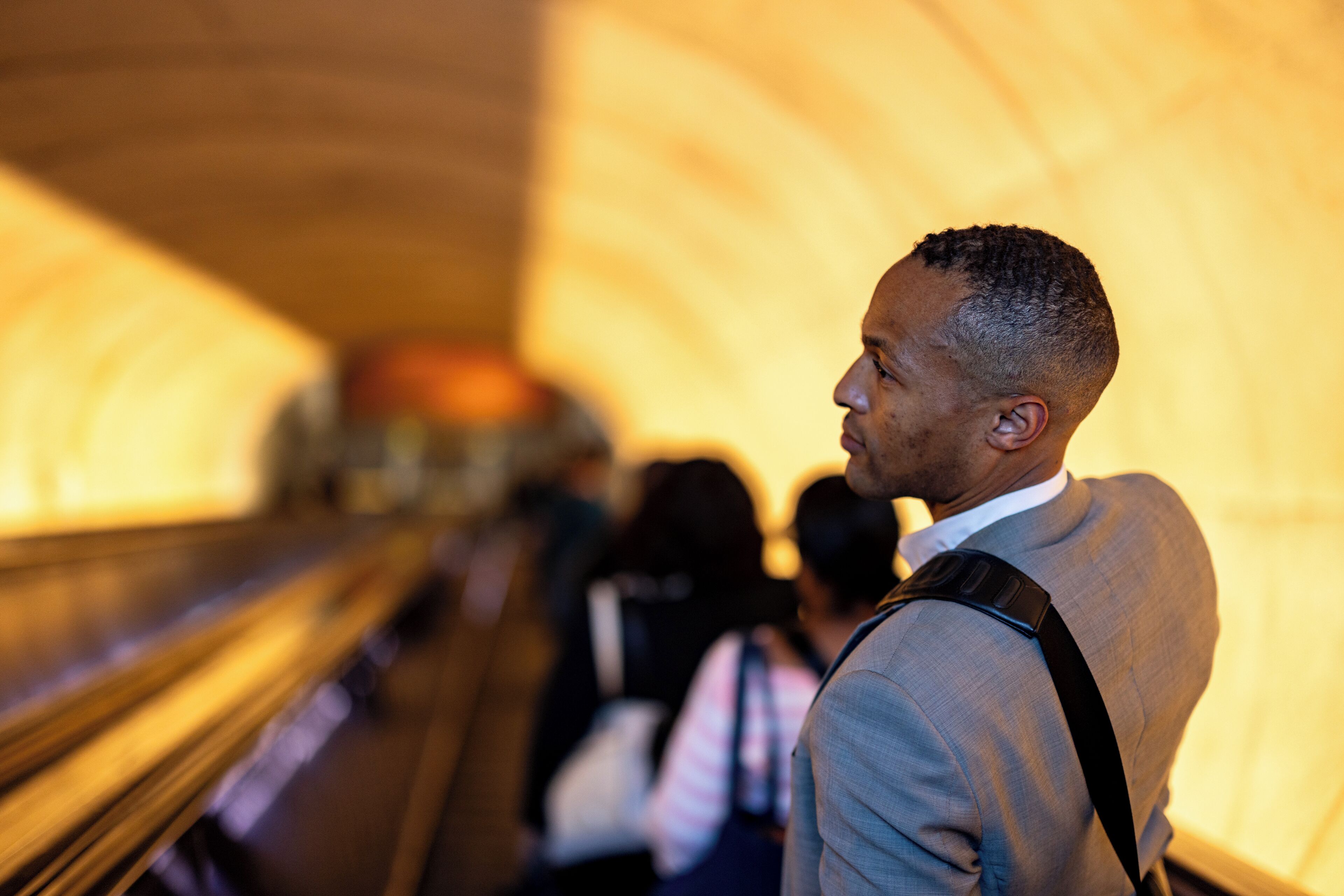 A man in a suit standing on an escalator in a well-lit, modern building with a curved ceiling.
