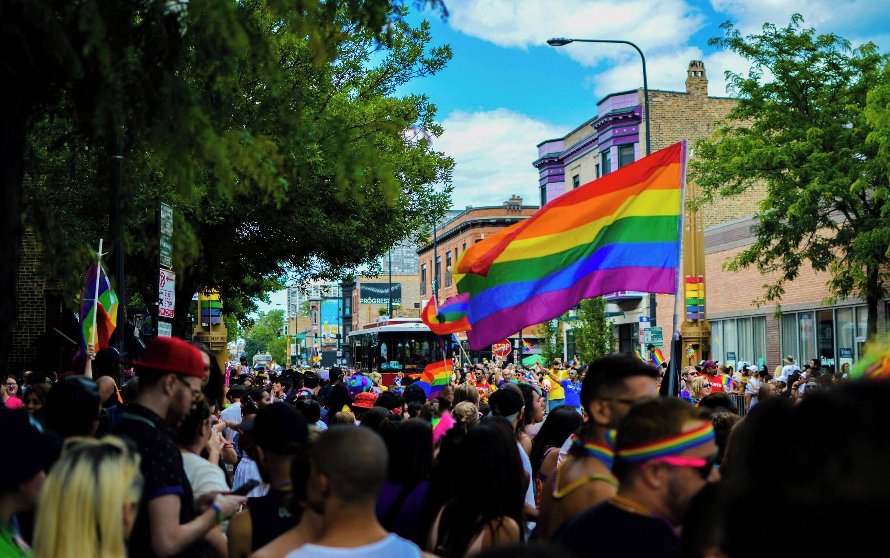 A crowded street with people holding rainbow flags, indicating a public event or parade.