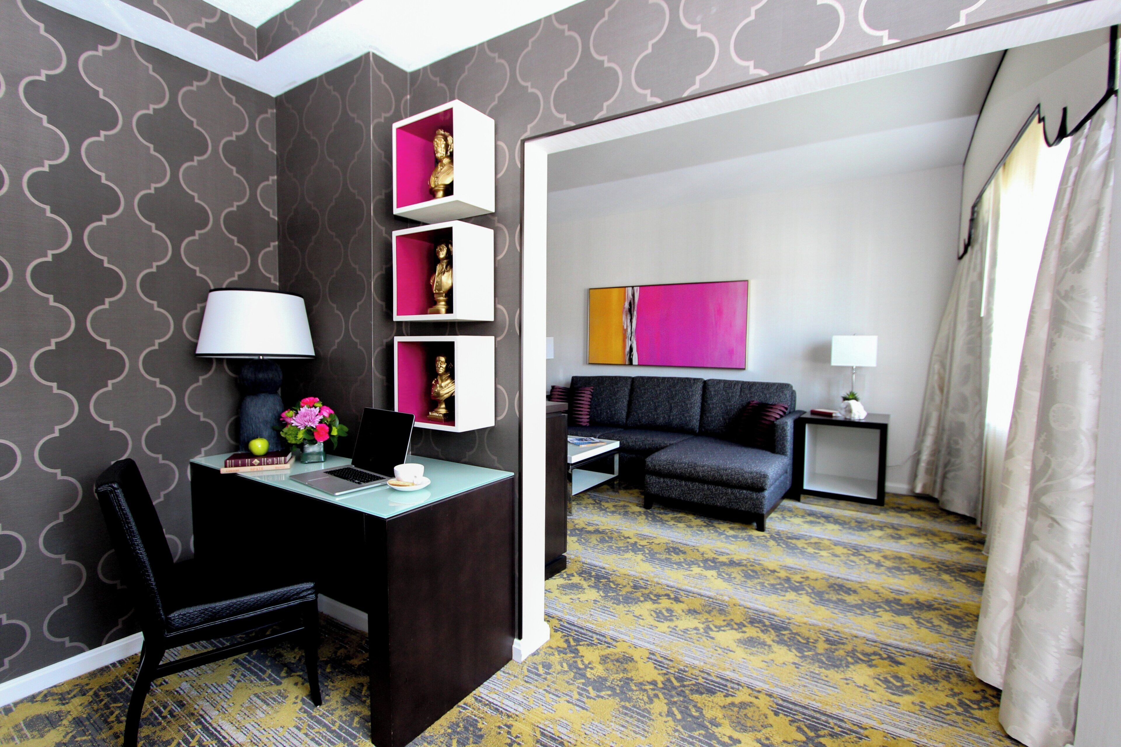 A modern hotel room with a desk, chair, and a sofa. There are decorative items on the walls and a painting on the wall.