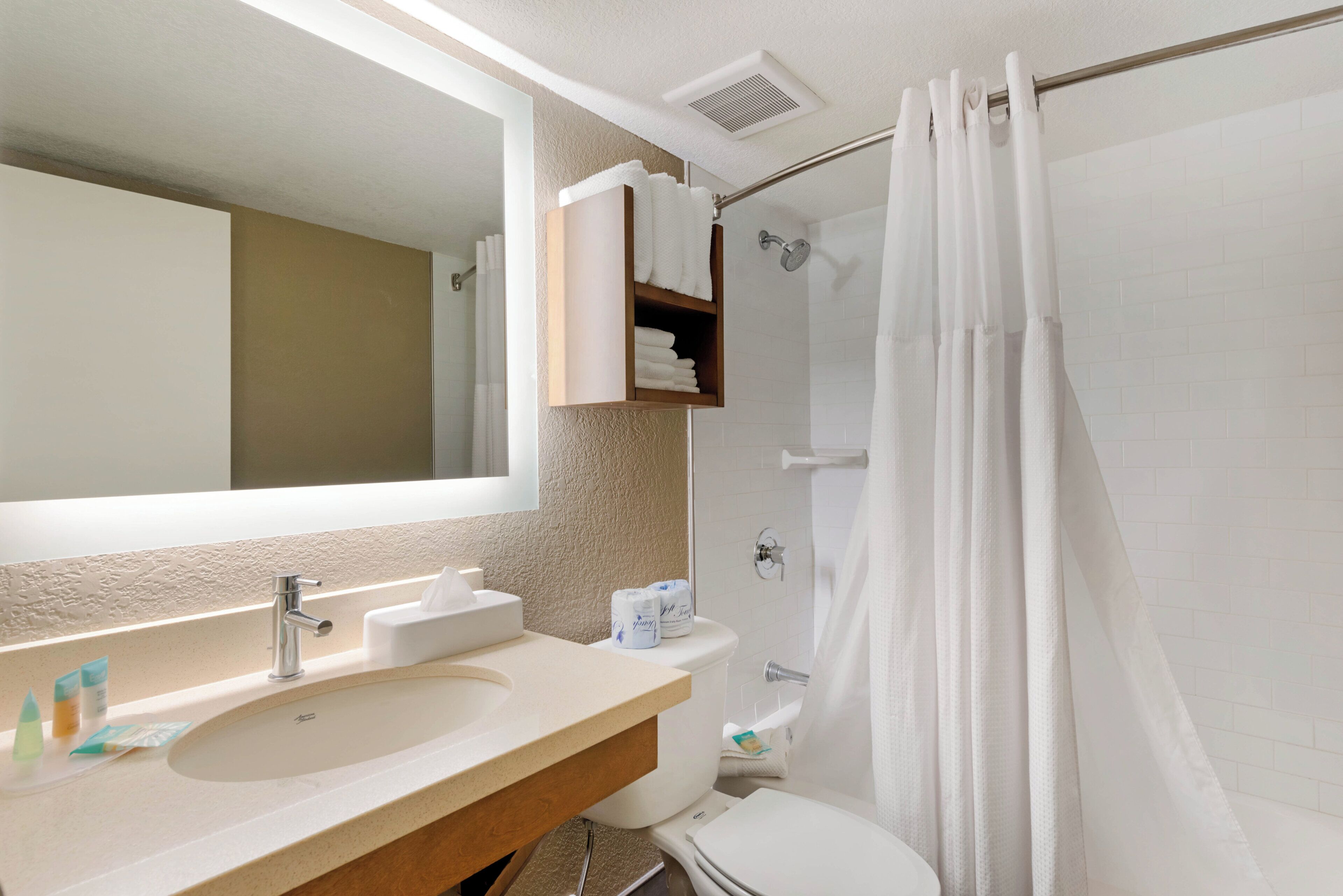 A bathroom with a large mirror, a sink, a toilet, and a shower area.