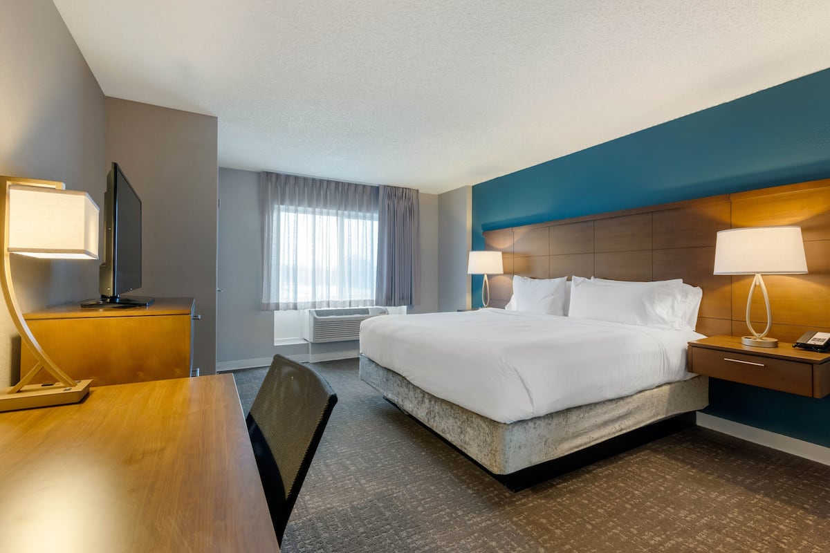 A hotel room with a large bed, a desk with a lamp, a TV, and a window with curtains.