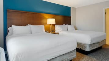 Habitación de hotel con dos camas, una mesita de noche con lámpara y una pared azul decorativa.