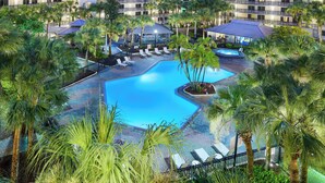 Un hotel con piscina rodeada de palmeras y sillones de descanso.
