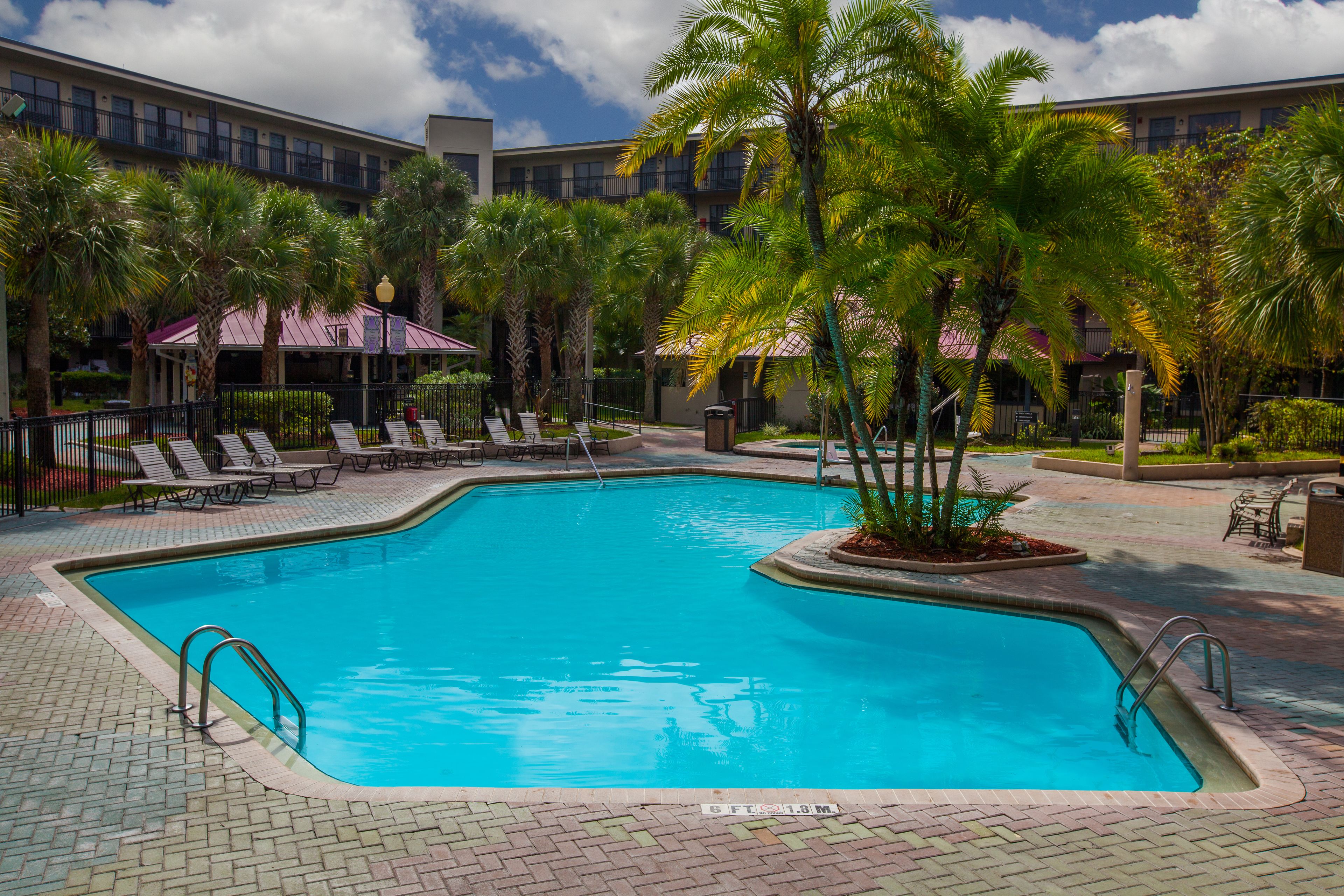 A swimming pool with lounge chairs and palm trees, surrounded by a building with balconies.