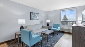 Un salon moderne comprenant un canapé, deux fauteuils, une table basse et une fenêtre donnant sur des arbres et des immeubles.